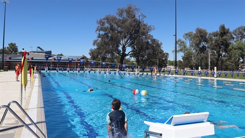 Wangaratta Sports & Aquatic Centre people swimming in blue heated outdoor 50 metre swimming pool with trees behind and blue sky