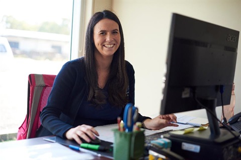 Women sitting at desk in front of desk top computer smiling 