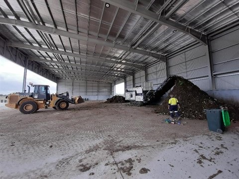 Inside large shed at Wangaratta Organics Plant with front end loader shifting compost near man in high visibility workwear
